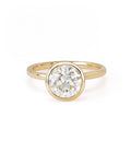 A round diamond solitaire ring with a bezel setting on a yellow gold band.