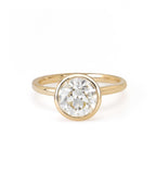 A round diamond solitaire ring with a bezel setting on a yellow gold band.