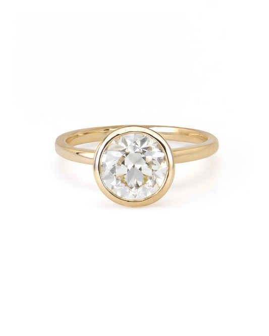 A round diamond solitaire ring with a bezel setting on a yellow gold band.