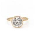 A round diamond solitaire engagement ring with a bezel setting on a yellow gold band.