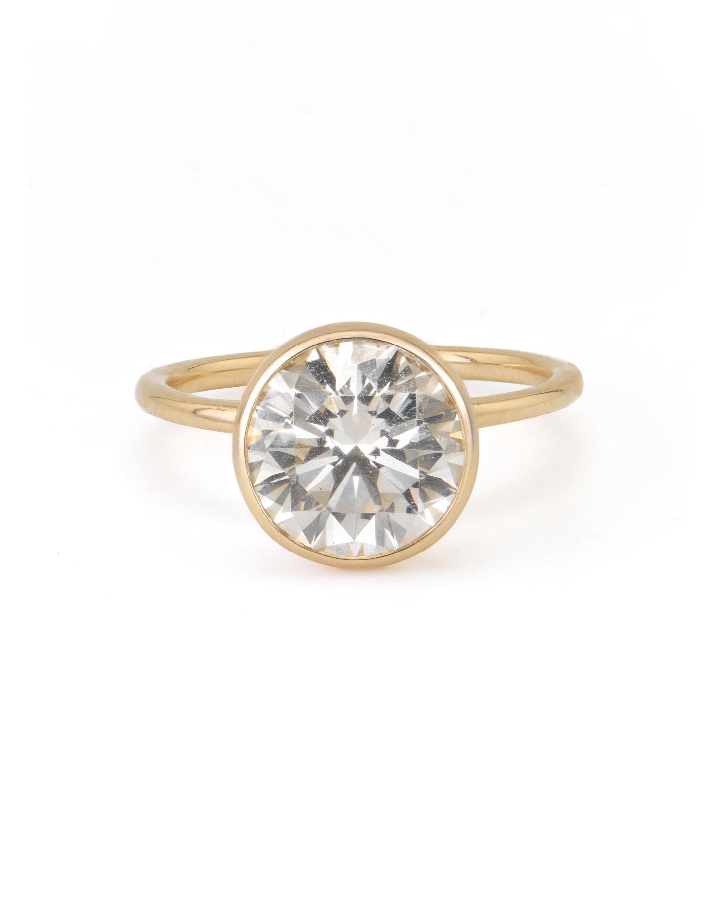 A round diamond solitaire engagement ring with a bezel setting on a yellow gold band.