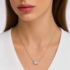A close-up of a woman wearing a delicate gold chain necklace with a small rectangular baguette-cut clear gemstone pendant, paired with a white V-neck top.