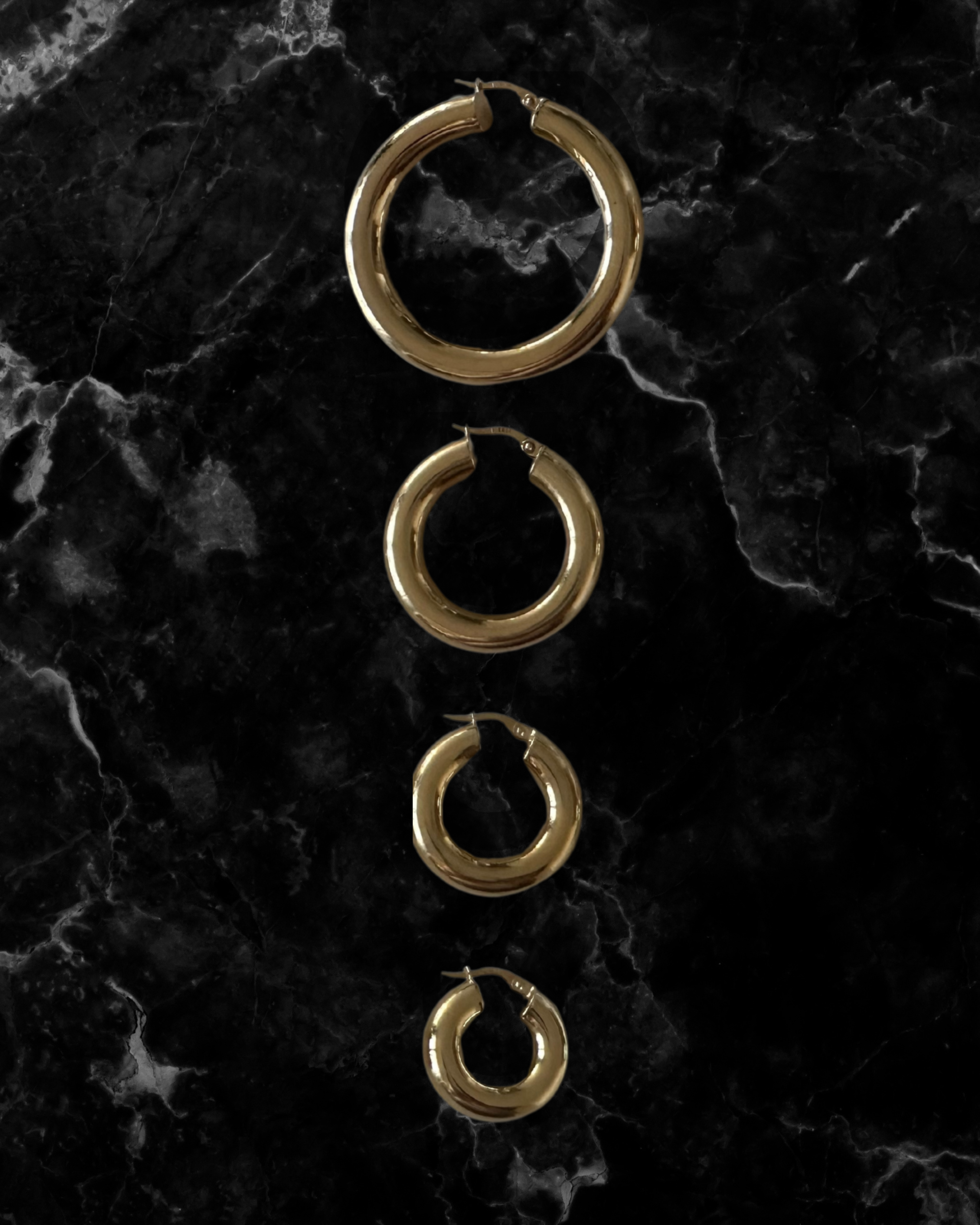 Set of gold hoop earrings on a dark marble surface