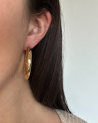 Close-up of a person wearing a gold hoop earring with a plain background