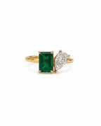 A yellow gold ring featuring a rectangular emerald-cut emerald and a pear-cut diamond on a white background.