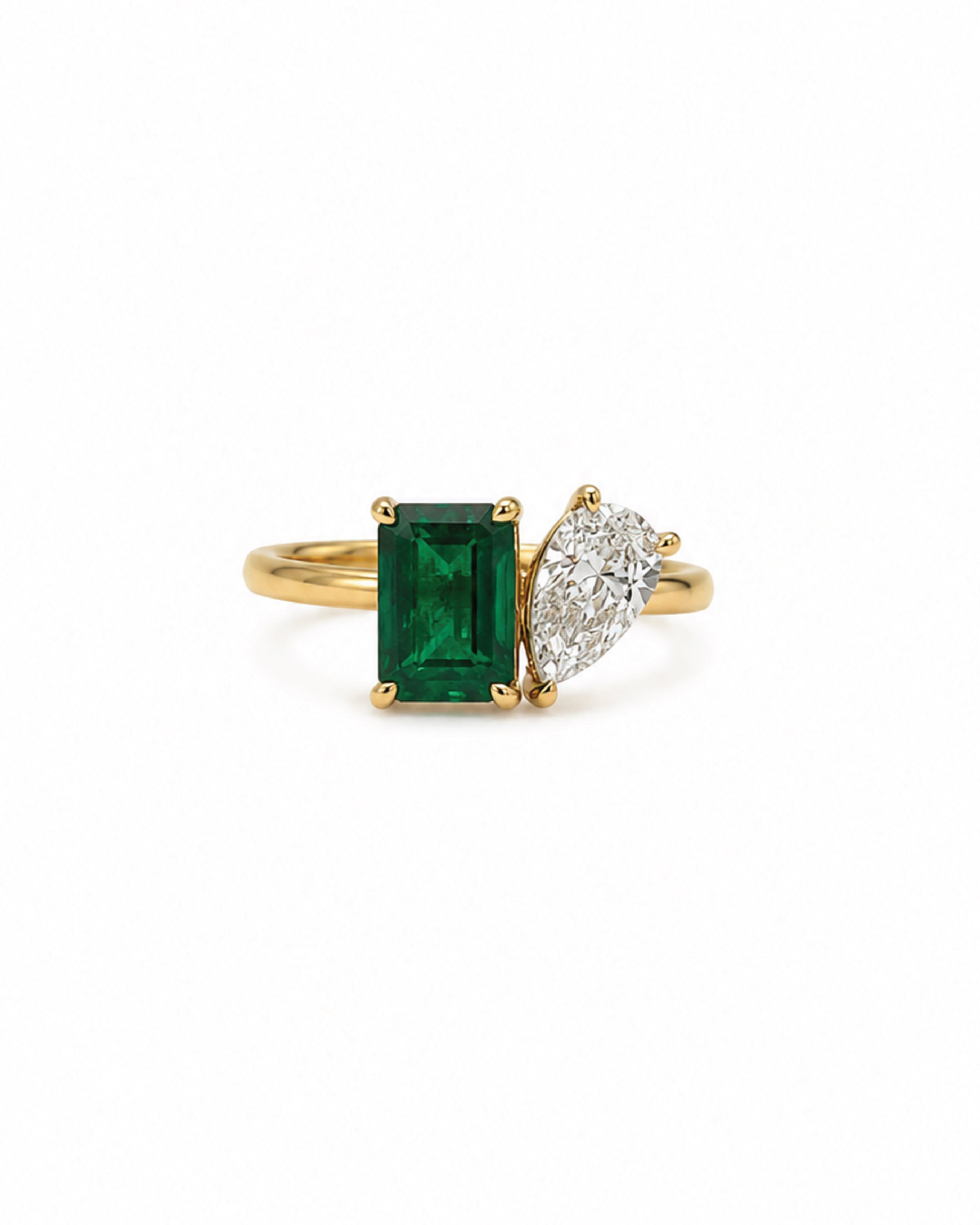 A yellow gold ring featuring a rectangular emerald-cut emerald and a pear-cut diamond on a white background.