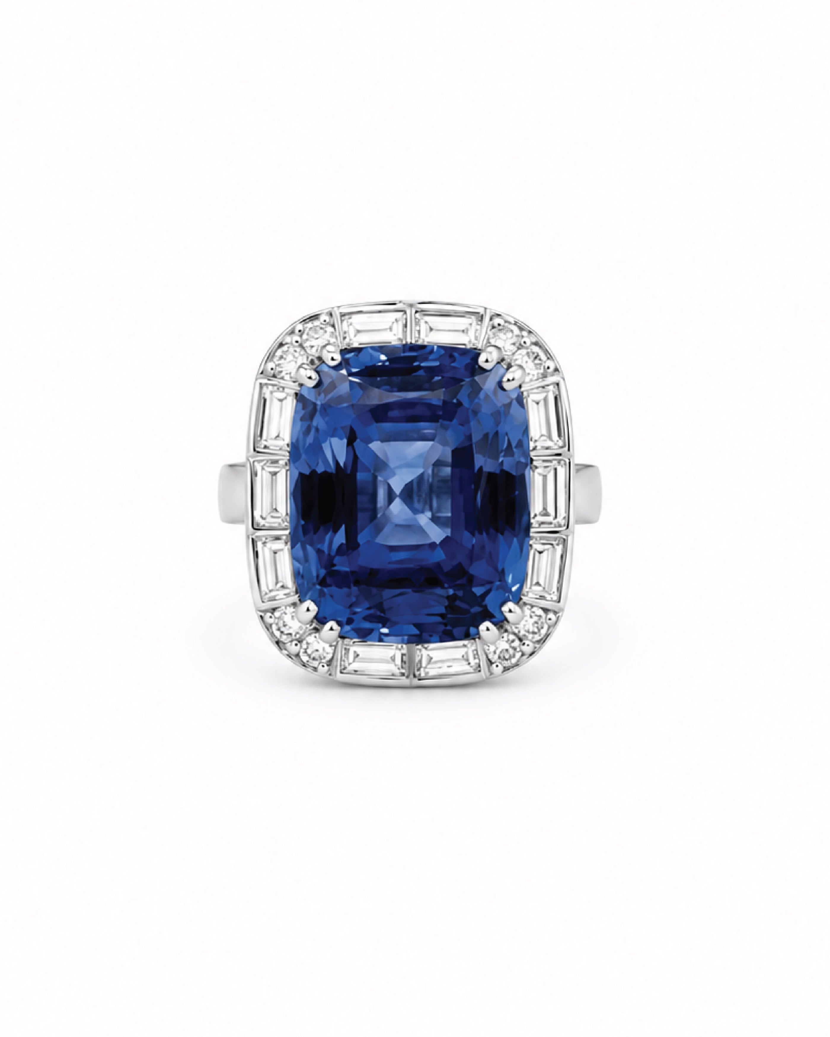 A white gold ring featuring a large cushion-cut deep blue sapphire gemstone surrounded by a halo of baguette and round diamonds, set against a plain white background.