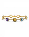 A gold link bracelet featuring four cushion-cut gemstones in bezel settings: purple amethyst, yellow citrine, light blue topaz, and a green-blue stone, accented with small pavé diamonds on a white background.