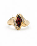 A gold ring featuring a marquise-cut garnet in the center, surrounded by small diamonds along the wave-like setting, on a plain white background.