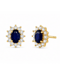 A pair of gold halo stud earrings featuring oval-cut dark blue sapphires surrounded by small clear stones, shown on a plain white background.