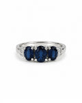 A white gold ring featuring three oval-cut deep blue sapphires in the center, flanked by small diamonds on a plain white background.