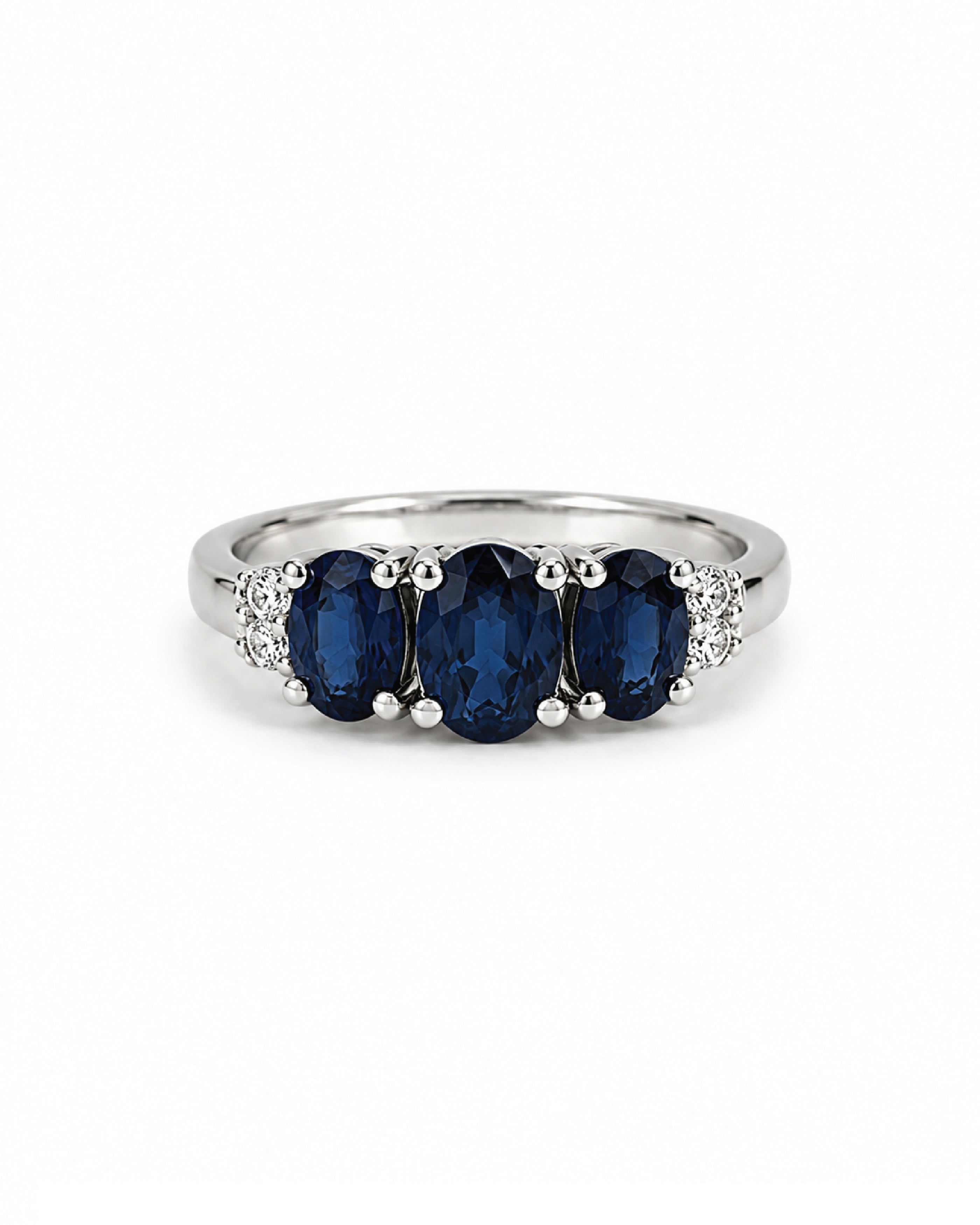 A white gold ring featuring three oval-cut deep blue sapphires in the center, flanked by small diamonds on a plain white background.